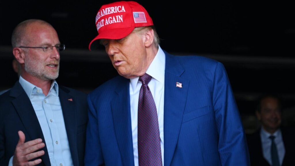 FCC Commissioner Brendan Carr standing next to and speaking to Donald Trump, who is wearing a "Make America Great Again" hat.