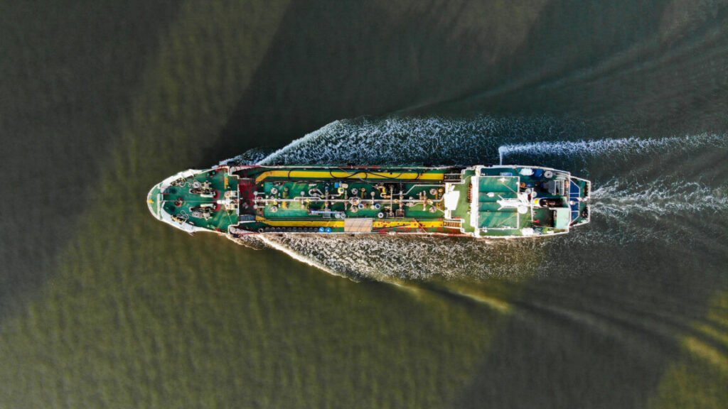 A top-down aerial view of a tanker ship churning through the water with a visible wake. Oil tankers and gas tankers were affected by the closure of the Strait of Hormuz, leading to a global energy crisis stemming from the war in the Middle East.