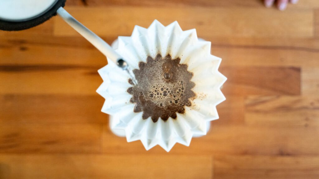 Hot water being poured into a pour-over container, seen from above, as the coffee grounds are blooming.