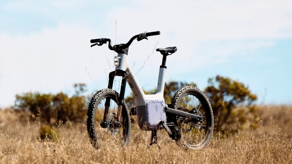 First look: Also’s upcoming e-bike disconnects the pedals and wheels A field with high grass, and a bicycle sitting in the middle of it. The bicycle has a distinctive square assembly in the region where the cranks are located on a normal bicycle.