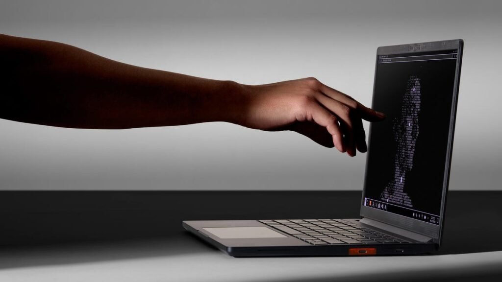 A hand reaches out to the Framework Laptop 13 Pro display. A computer-generated face is on the screen.