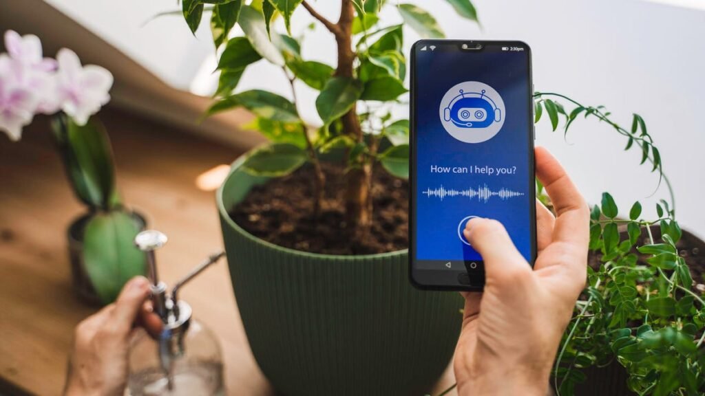 I Used AI to Help Me Stay Ahead of Home Maintenance. Here’s How A person holds a phone with a chatbot while preparing to water a plant.