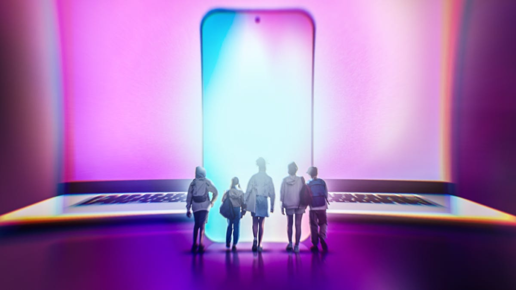 A group of teens standing before a glowing smartphone and laptop