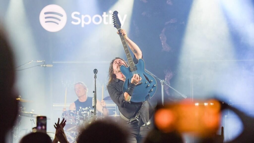 Spotify Champions Live Music With Independent Music Venue Deal Dave Grohl holds a blue guitar in front of him as Foo Fighters play on stage.