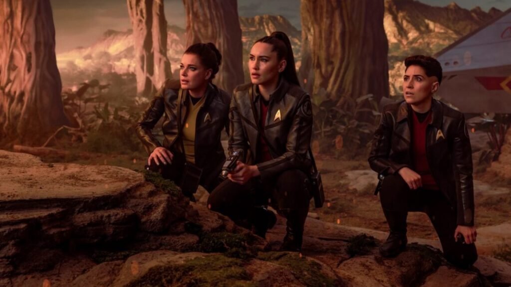 Enterprise crew members on an alien planet hunched down and surveying the terrain