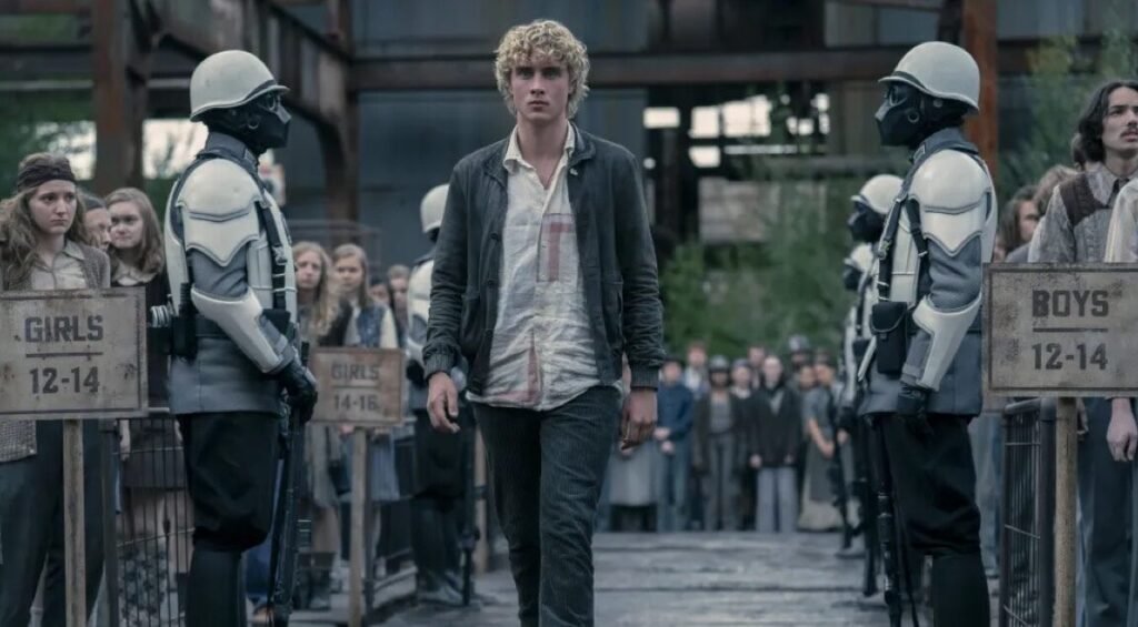 young man with tousled blonde hair walking between two rows of potential tributes
