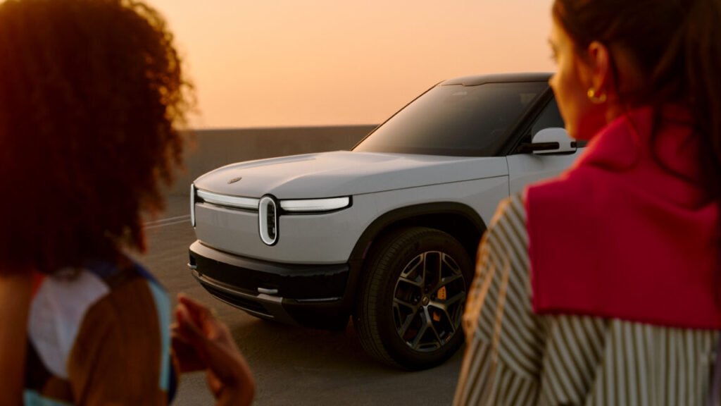 A white Rivian R2 with two women standing in front of it
