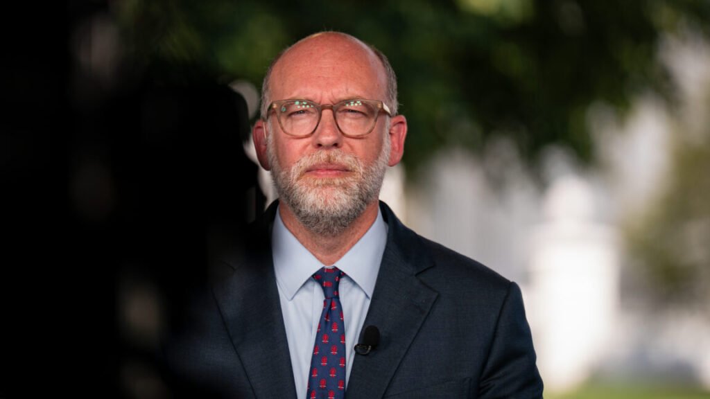 Image of a white man in a suit with glasses.