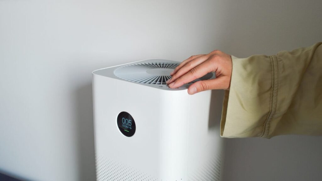 A hand touching the top of a white air purifier.