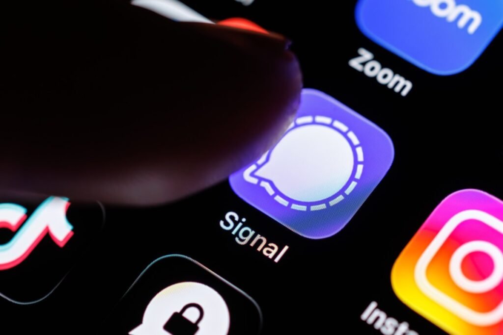 The Signal app logo can be seen on the display of a smartphone while a finger taps on the application icon.