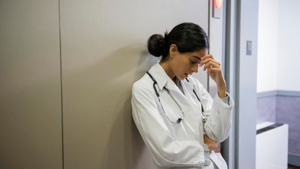 Stressed Indian doctor leaning on wall