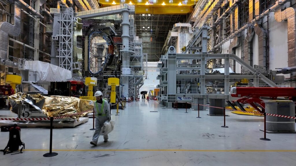 inside iter's tokamak assembly hall a high-cieling building filled with tokamak components and a worker walking by
