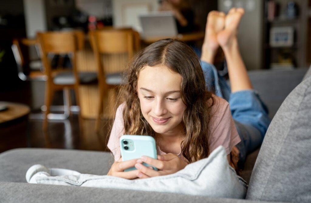 Teenage girl using her cell phone and smiling while lying on a couch