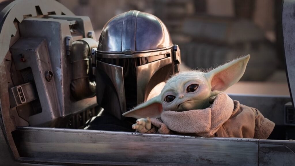 Review: The Mandalorian and Grogu is … fine mandolorian in full armor and helmet with little green yoda-like figure sitting in a spacecraft