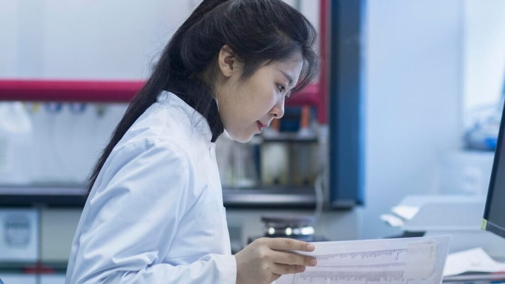 Scientist reading paper in lab in front of a computer