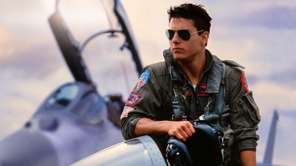 Stunning aerial footage still best thing about Top Gun at 40 young to cruise in fighter pilot uniform and sunglasses casually leaning against a fighter jet