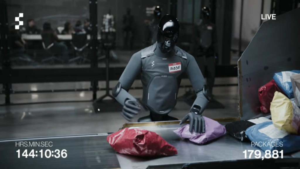 The Internet can’t stop watching Figure AI’s humanoid robots handling packages A humanoid robot with a gray body and black, reflective head stands next to a package sorting station while moving boxes and padded envelopes onto a conveyor belt.
