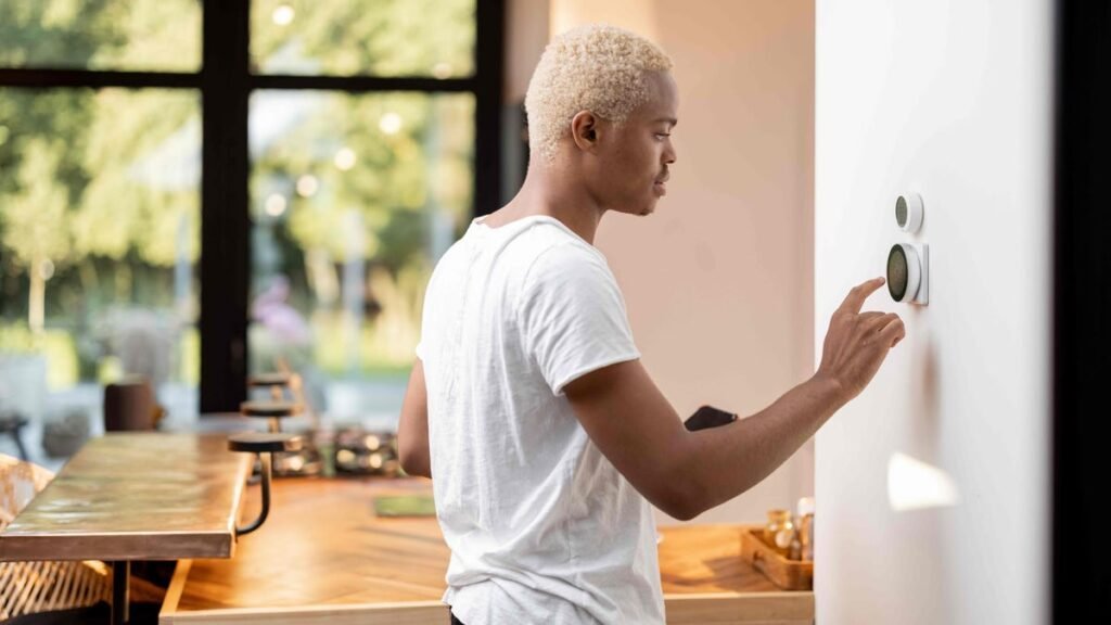 A man in a white shirt taps a smart thermostat on a white home wall.