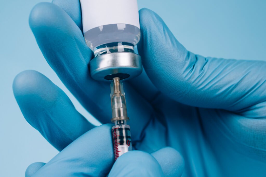 Blue-gloved hands using a needle and bottle to give a vaccine.