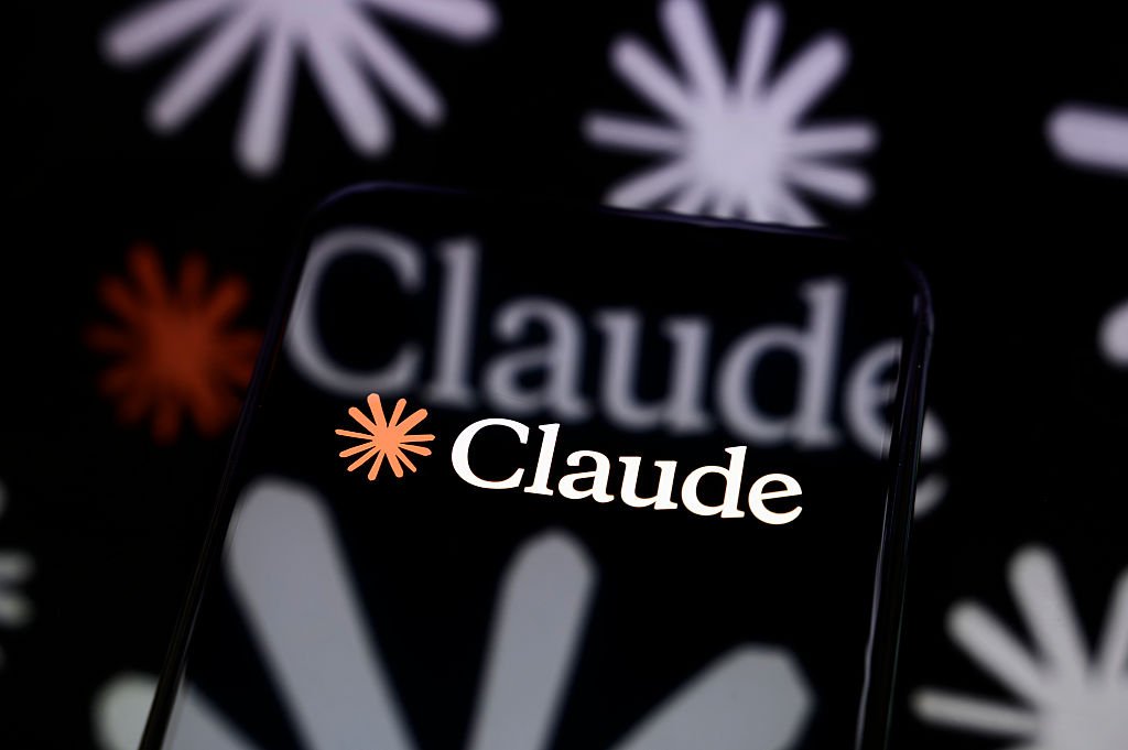 Anthropic is turning Claude Code’s auto mode on by default The Claude logo is displayed on a smartphone screen placed on a reflective surface onto which a multitude of Claude logos are projected.