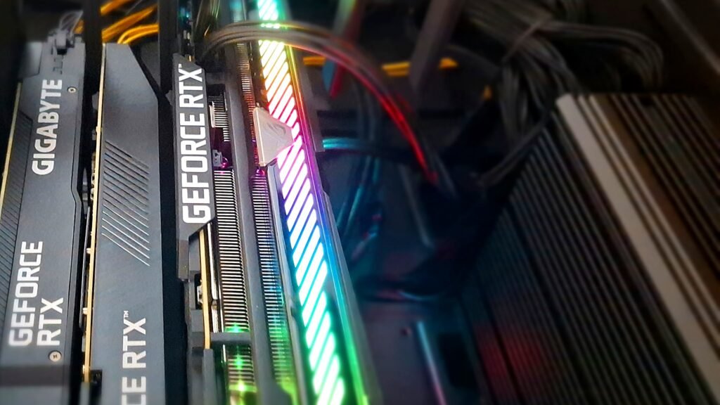 Three GPUs stacked inside an open computer case, lit by a multicoloured RGB light bar running between the heatsinks