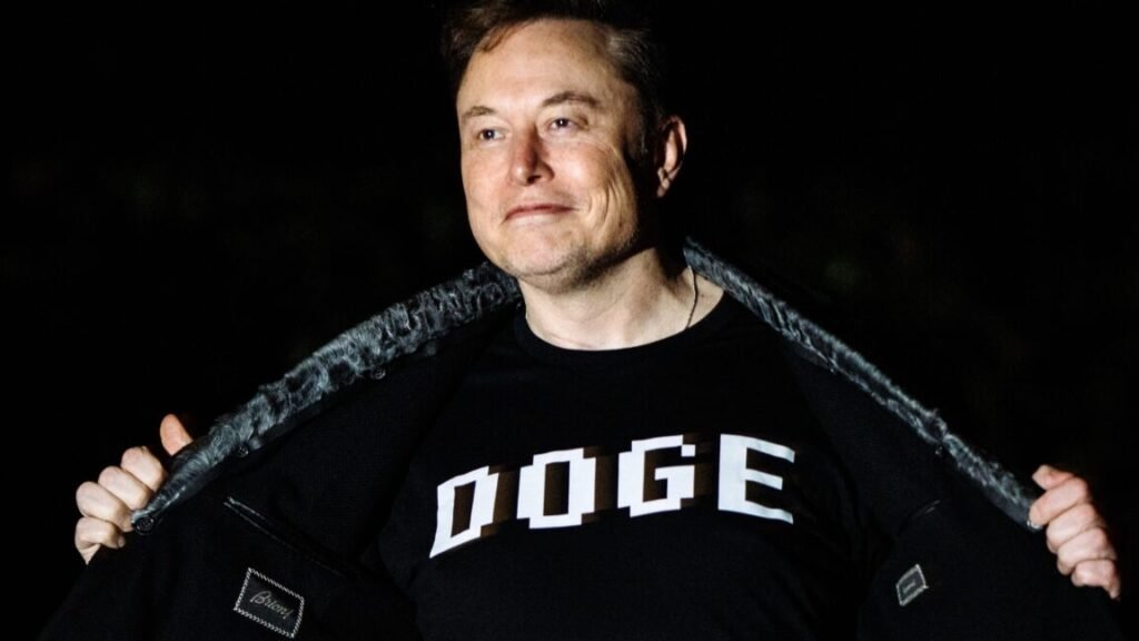 Elon Musk wearing a T-shirt with the word "DOGE" printed on the front.