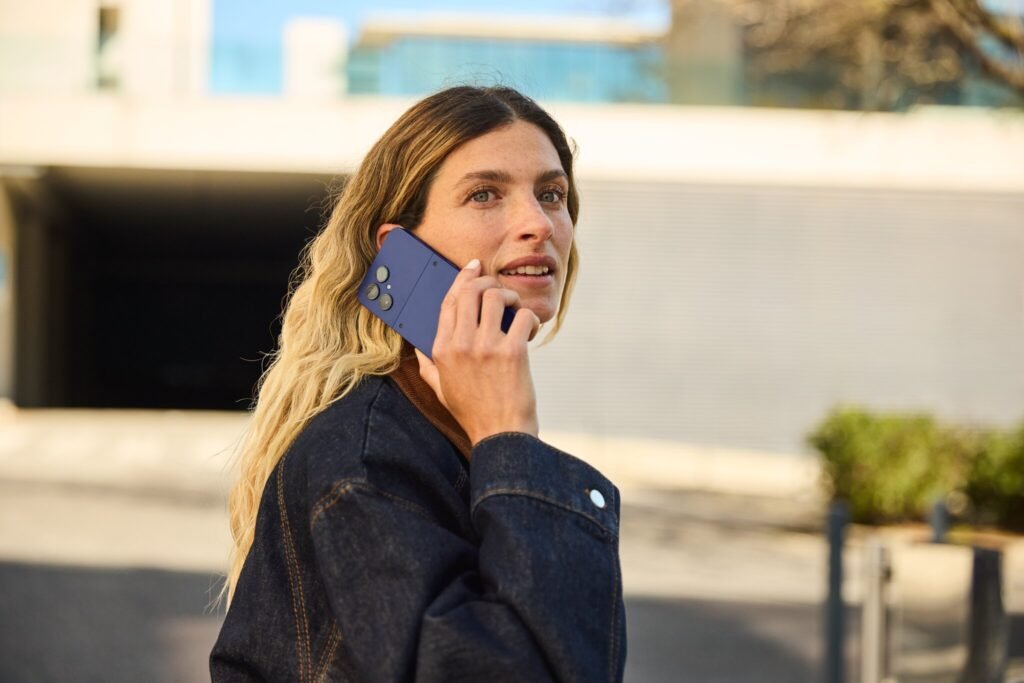Fairphone’s Repairable Smartphones Debut in the US With the 6 Plus A woman holds a blue smartphone to her ear as she's outside.