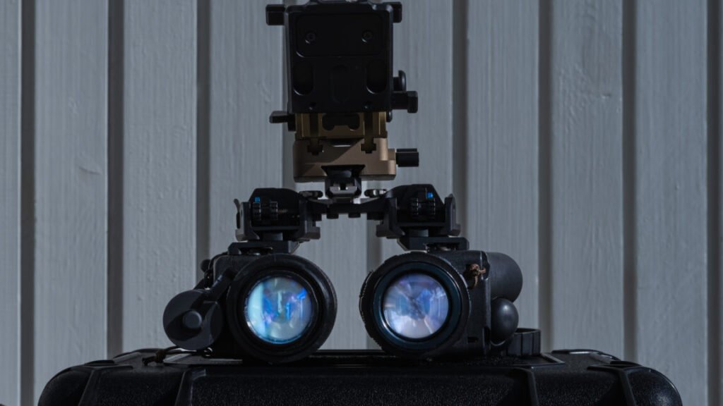 Front view of modern binocular night vision goggles (NVG) with a mount, sitting on top of a black protective case.