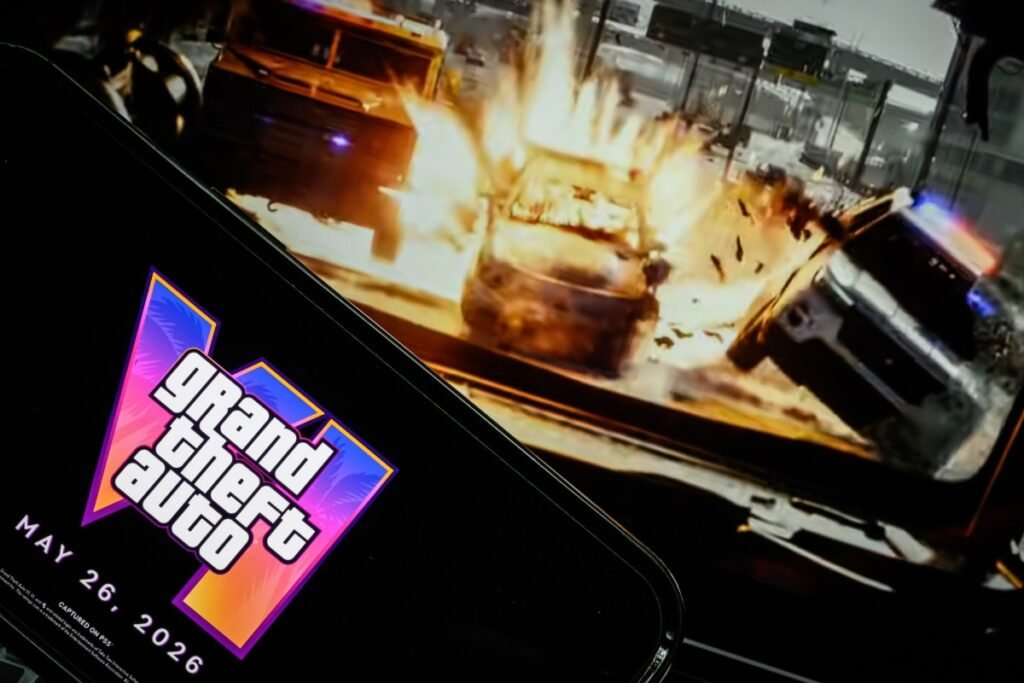 In this photo illustration, a phone displaying the Grant Theft Auto VI logo and new release date is shown in front of a screen displaying the second official trailer for the game.