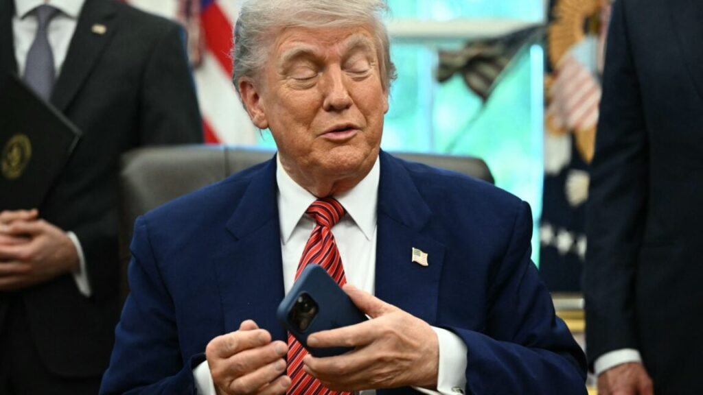 President Trump sitting at his desk in the White House while holding a smartphone in his left hand.