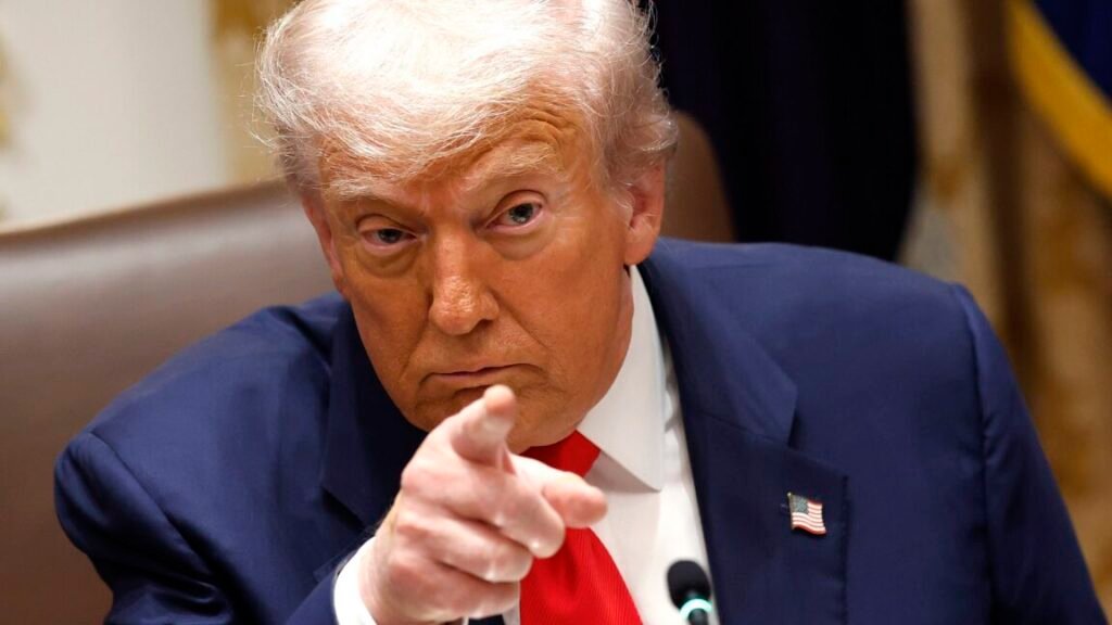 President Donald Trump sits in a chair and points with his right index finger during a meeting.