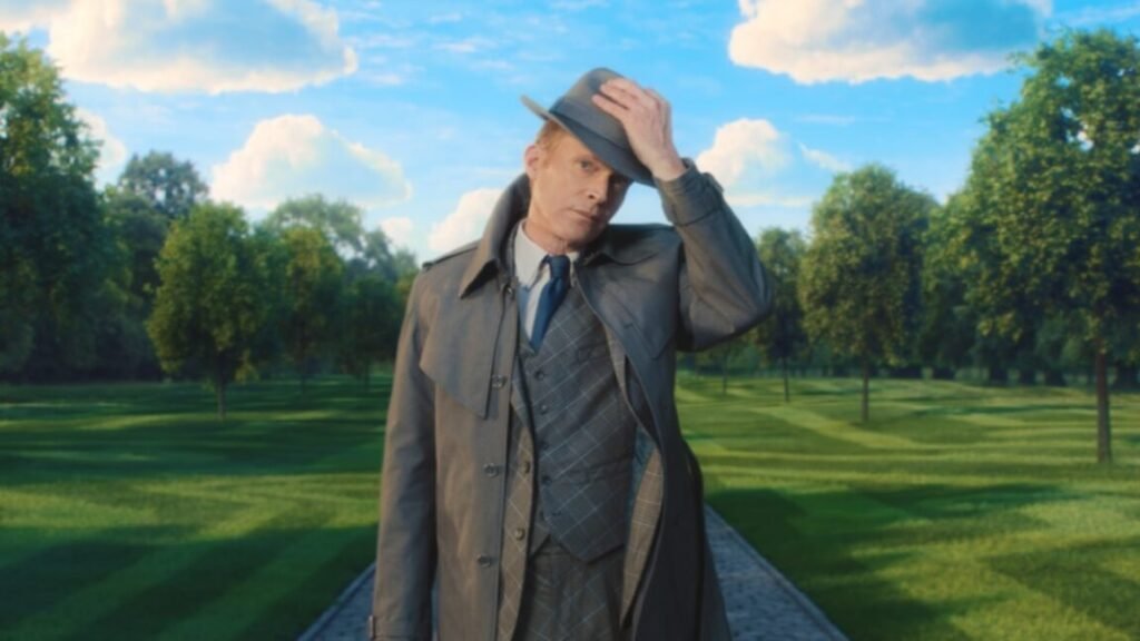 still image showing a man in great raincoat and hat standing against an idyllic background of green flora and blue skies