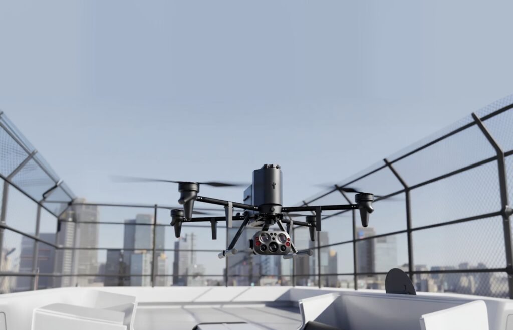 A black drone hovers atop a building rooftop with a cityscape in the background.