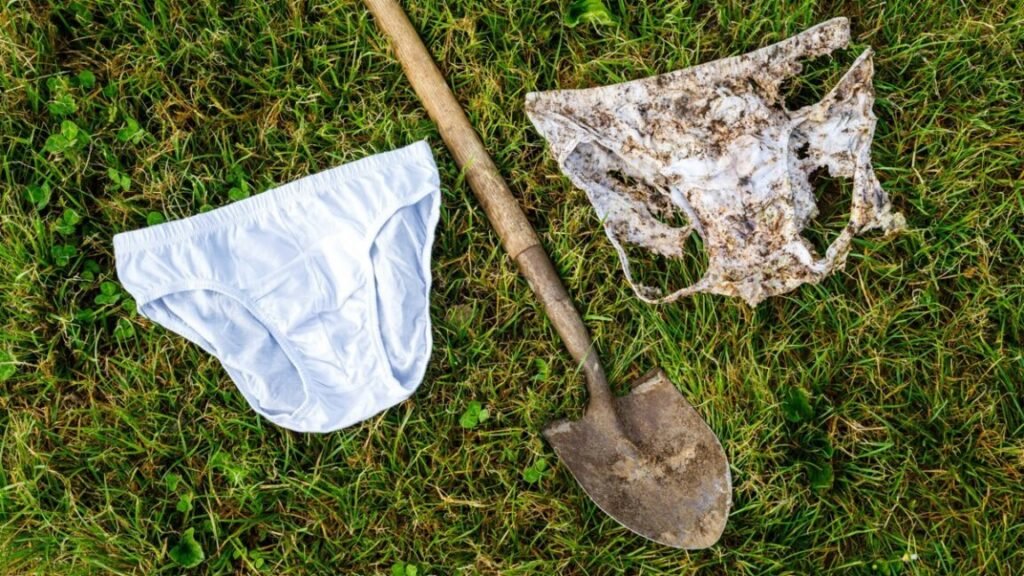 A new pair of cotton underwear, a pair that's partially buried in the ground, and a shovel lying between them in the grass.