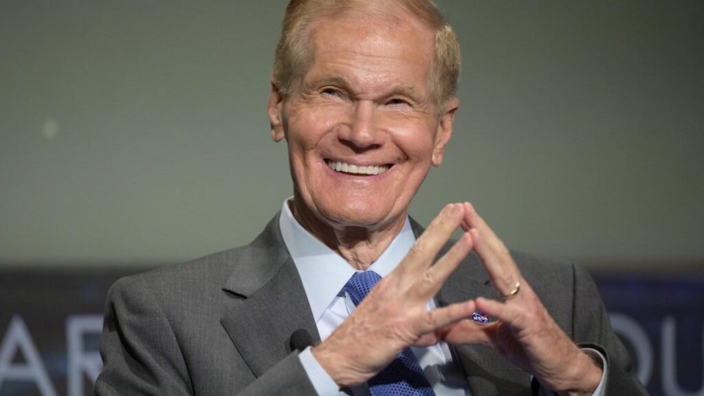 An older man in a suit smiles.