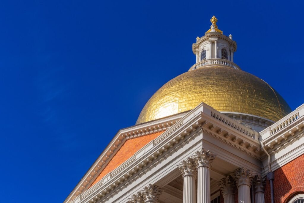 The gold dome of the Massachusetts State House stands against a blue sky.