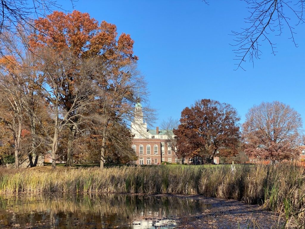A wooded lake, with a stately Georgian brick building visible in the distance.