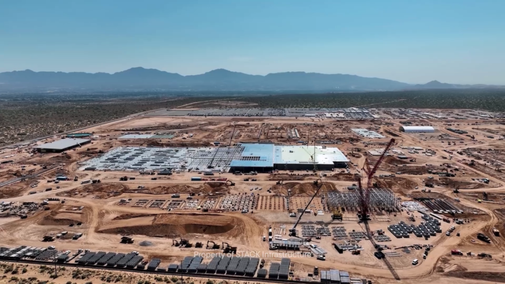 The Project Jupiter data center construction site in New Mexico as seen in a video posted in July 2026. The overhead camera angle shows a partially completed main building surrounded by cleared land, construction cranes and stacks of building materials.