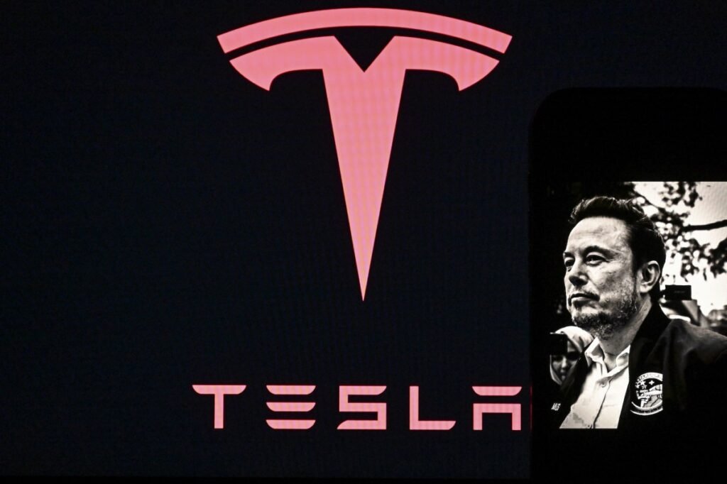 In this photo illustration, Tesla logo is seen on a screen, while an image of Tesla CEO Elon Musk is displayed on a mobile phone